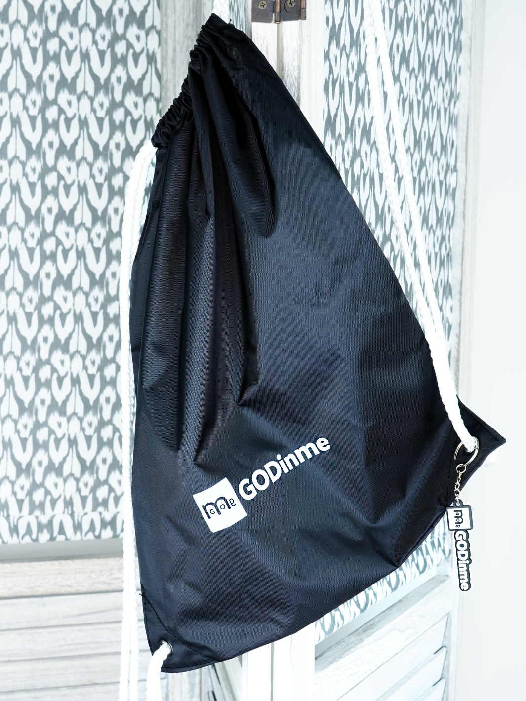 Soft yet durable Black nylon bag with thick White drawcord  and GODinme keychain attached. GODinme logo and name printed on front.