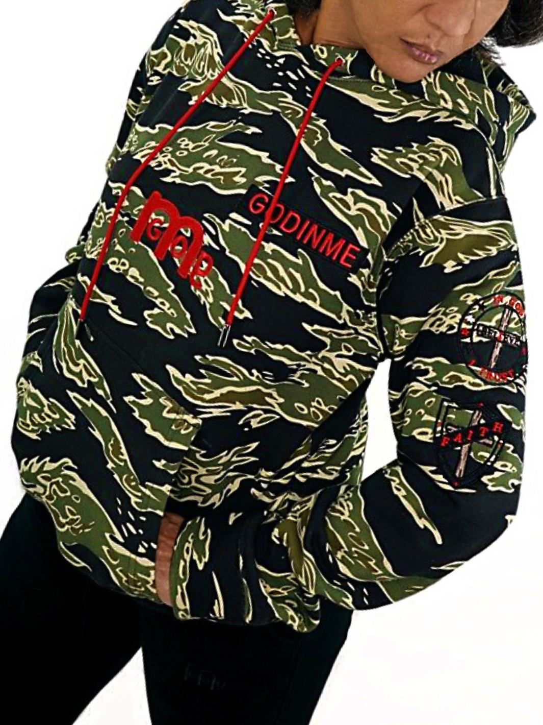 A model wearing a tiger stripe camouflage pattern hoodie, featuring red drawstrings, red embroidered GODinme logo mid-chest, Embroidered GODinme nameplate, and two embroidered faith driven patches on left sleeve.