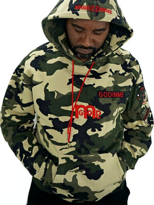 Male model wearing a camouflage pullover hoodie with a big bold red GODinme logo mid chest and embroidered  in red ROMANS 12 : 21 on hood. 